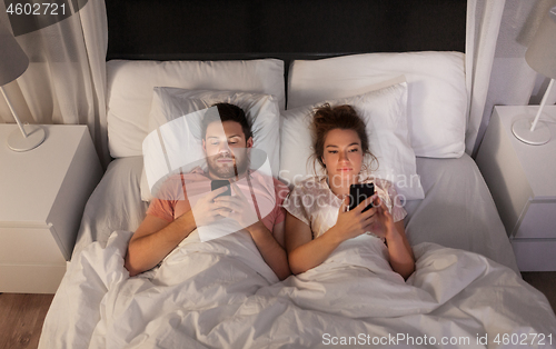 Image of couple using smartphones in bed at night