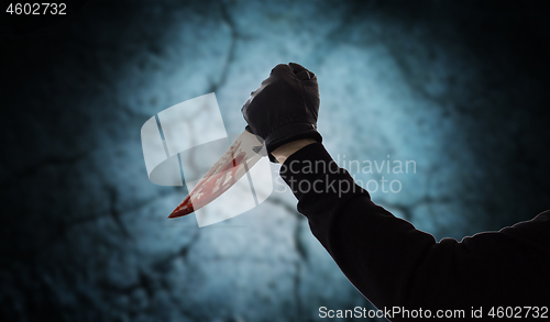 Image of hand with blood on knife over dark background