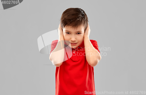 Image of stressed boy in red t-shirt closing ears by hands