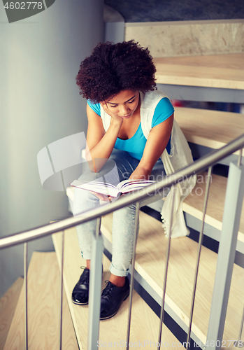 Image of african student girl reading book on stairs