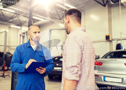 Image of auto mechanic with clipboard and man at car shop