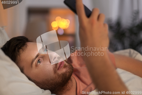 Image of young man with smartphone in bed at night