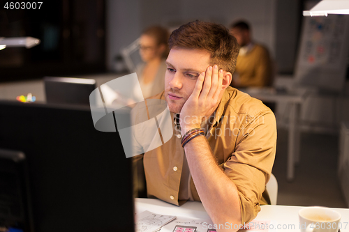 Image of tired or bored man with computer at night office