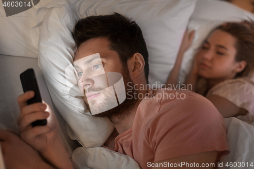 Image of man using smartphone while girlfriend is sleeping