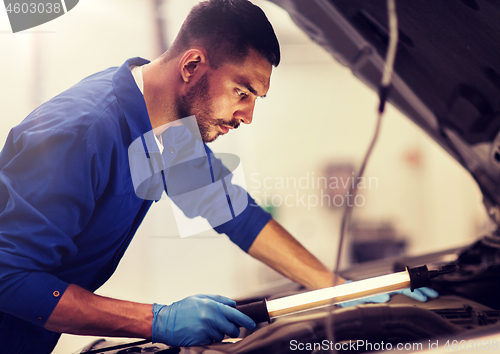 Image of mechanic man with lamp repairing car at workshop