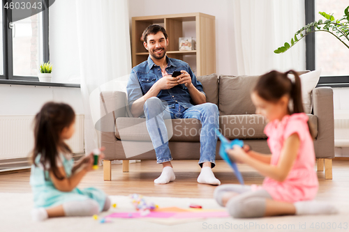 Image of father with smartphonew and daughters at home