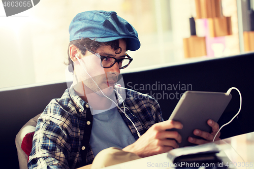 Image of man with tablet pc and earphones sitting at cafe