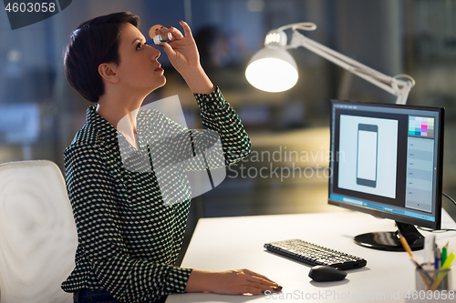 Image of female designer using eye drops at night office