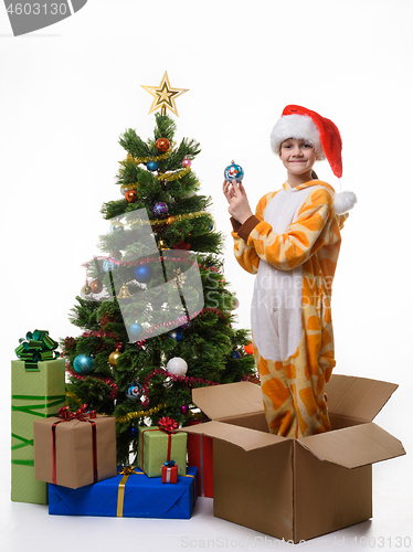Image of The girl stands in a box of Christmas tree toys dressing up the Christmas tree and looked cheerfully in the frame