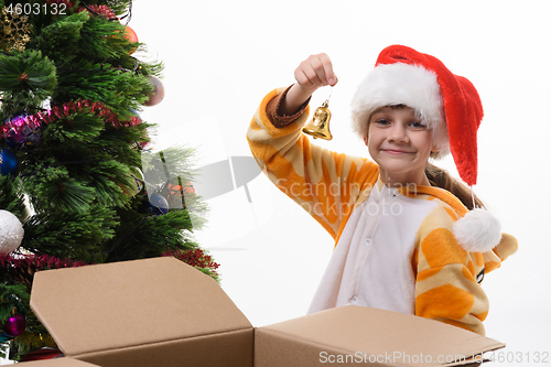 Image of The girl took out a toy bell out of the box and is going to hang it on the Christmas tree