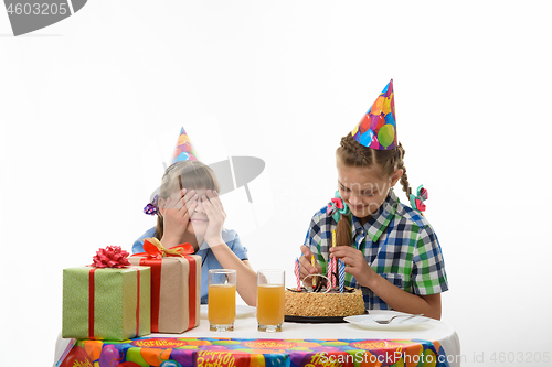 Image of A girl puts candles on a birthday cake, the other closed her eyes