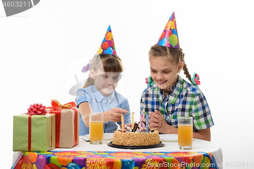 Image of children light candles with a match on the cake, at the table at the birthday party
