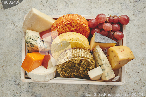 Image of Fresh and delicious different kinds of cheeses placed in wooden crate with grapes