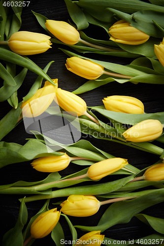 Image of Yellow tulips placed on black table. Top view with flat lay