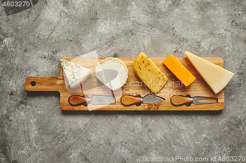 Image of Assortment of various kinds of cheeses served on wooden board with fork and knives