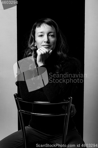 Image of Cute girl sits on a bar chair and clouds her hands on the back of a chair, black and white photo