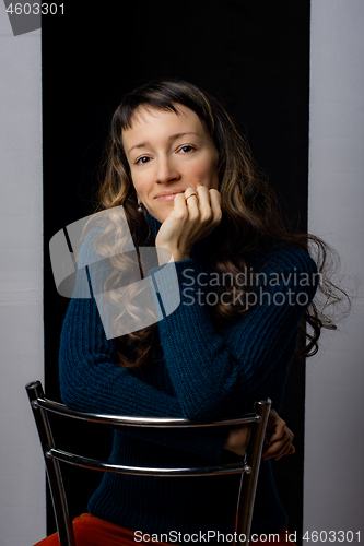 Image of Cute girl sits on a bar chair and clouds her hands on the back of a chair, black gray background