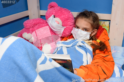 Image of Girl and plush toy in medical masks in bed read a book, and looked into the frame