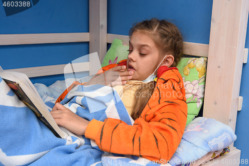 Image of Sick girl sneezes lying in bed and reading a book