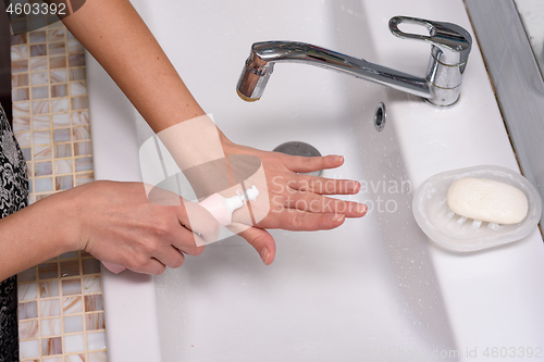 Image of Girl applies cream on skin of hands in the bathroom