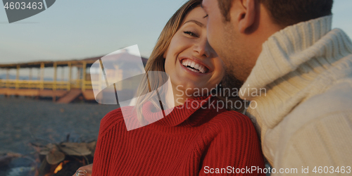 Image of Loving Young Couple Sitting On The Beach beside Campfire drinkin