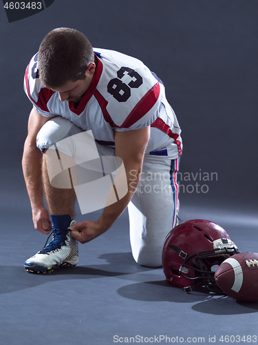 Image of American Football Player tie his shoe laces isolated on gray