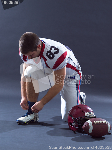 Image of American Football Player tie his shoe laces isolated on gray