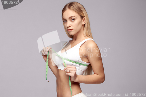 Image of Portrait of beautiful young woman measuring her leg size with tape measure.