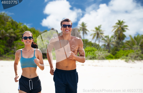 Image of couple in sports clothes running along on beach