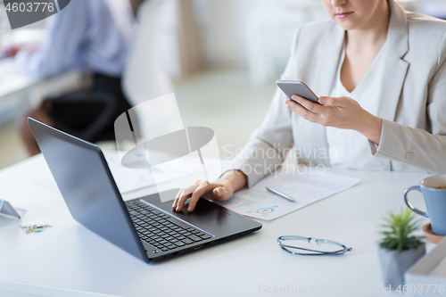 Image of businesswoman with smartphone and laptop at office