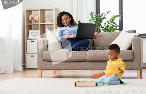 Image of mother with laptop looking at baby with toy blocks