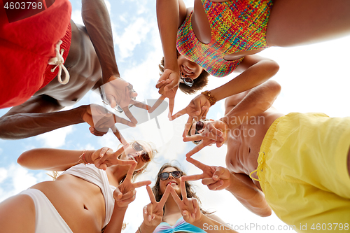 Image of happy friends showing peace in circle on beach