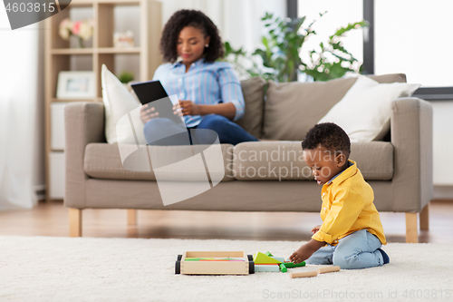 Image of baby playing toy blocks and mother using tablet pc