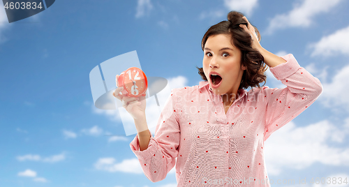 Image of shocked young woman in pajama with alarm clock