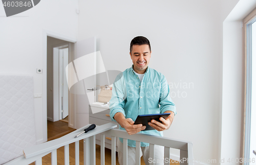 Image of father with tablet pc assembling baby bed at home