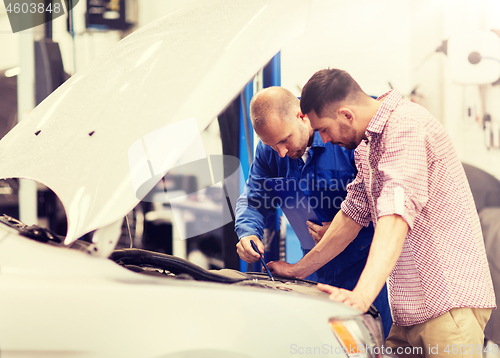 Image of auto mechanic with clipboard and man at car shop