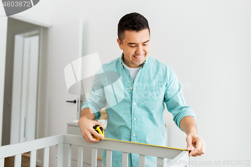 Image of father with tablet pc and ruler measuring baby bed