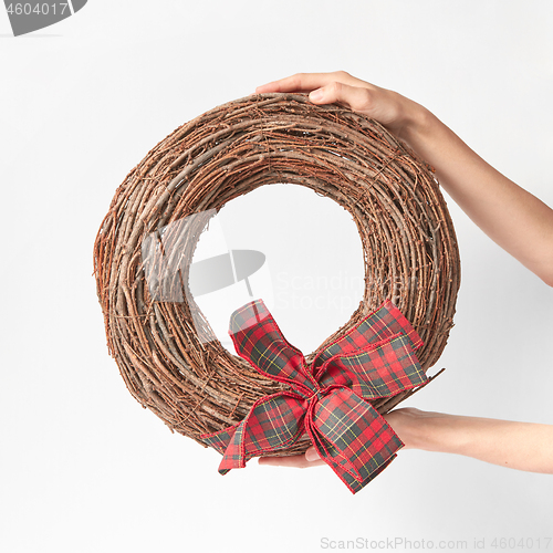 Image of Woman\'s hands hold round wreath from dry twigs with bow.