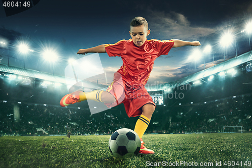 Image of Young boy with soccer ball doing flying kick at stadium