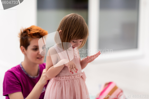 Image of young mother helping daughter while putting on a dress