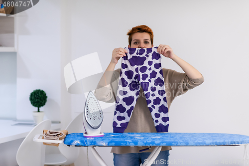 Image of Red haired woman ironing clothes at home