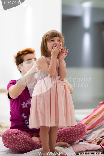 Image of young mother helping daughter while putting on a dress