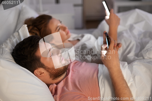 Image of couple using smartphones in bed at night