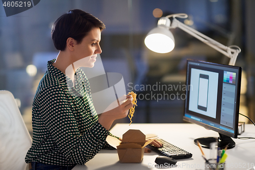 Image of female designer eating and working at night office