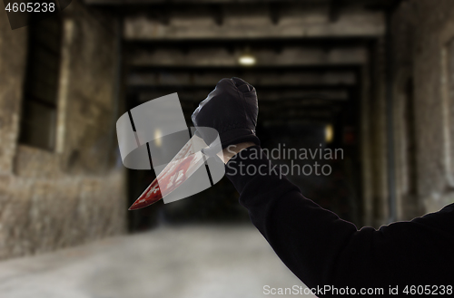 Image of hand in glove with bloody knife over dark gateway