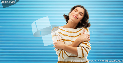 Image of happy woman in striped pullover hugging herself