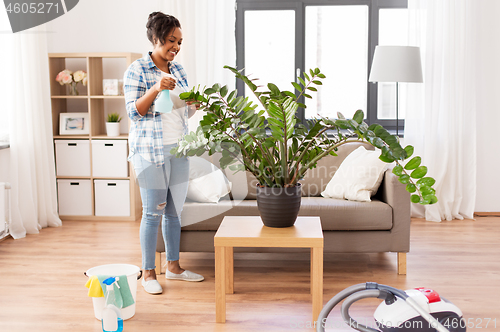 Image of happy african woman spraying houseplants at home