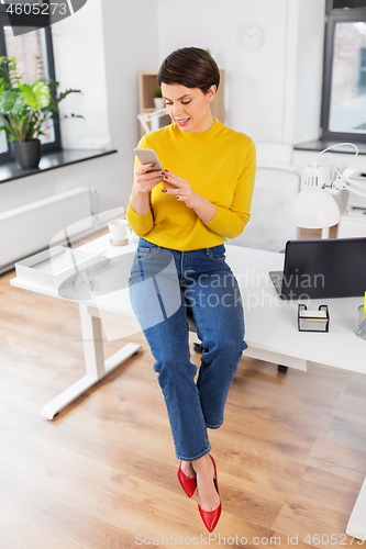 Image of happy woman with smarthone sitting on office desk