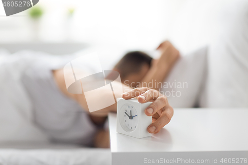 Image of close up of man in bed reaching for alarm clock