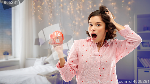 Image of shocked young woman in pajama with alarm clock